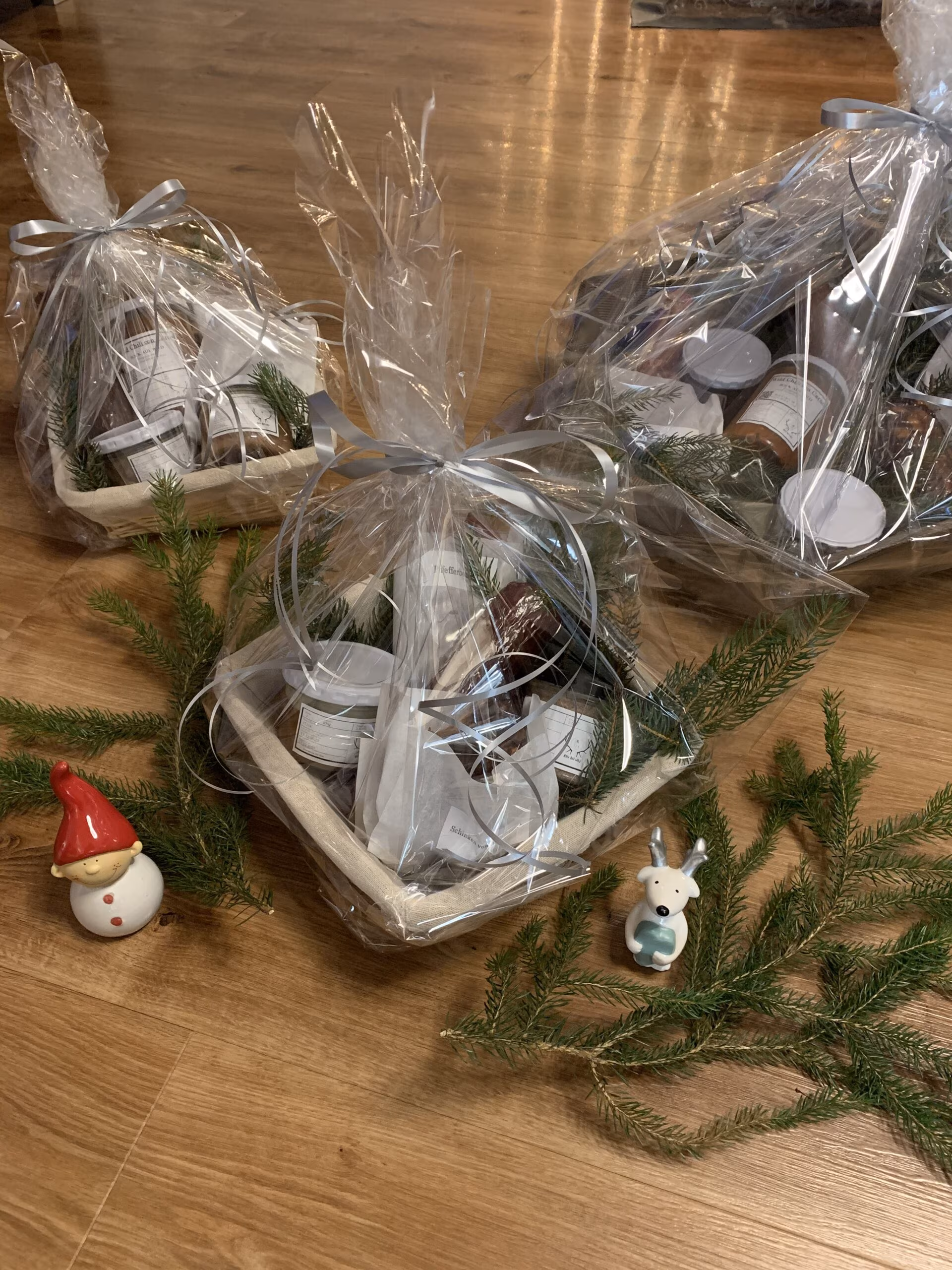 Zwei in Folie verpackte Geschenkkörbe mit Tannenzweigen auf einem Holztisch