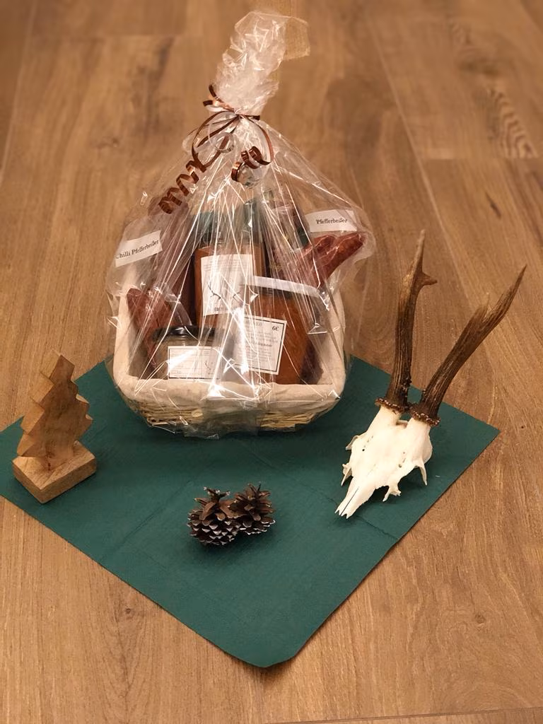 In Folie verpackter Geschenkkorb neben einem Geweih auf grünem Tuch