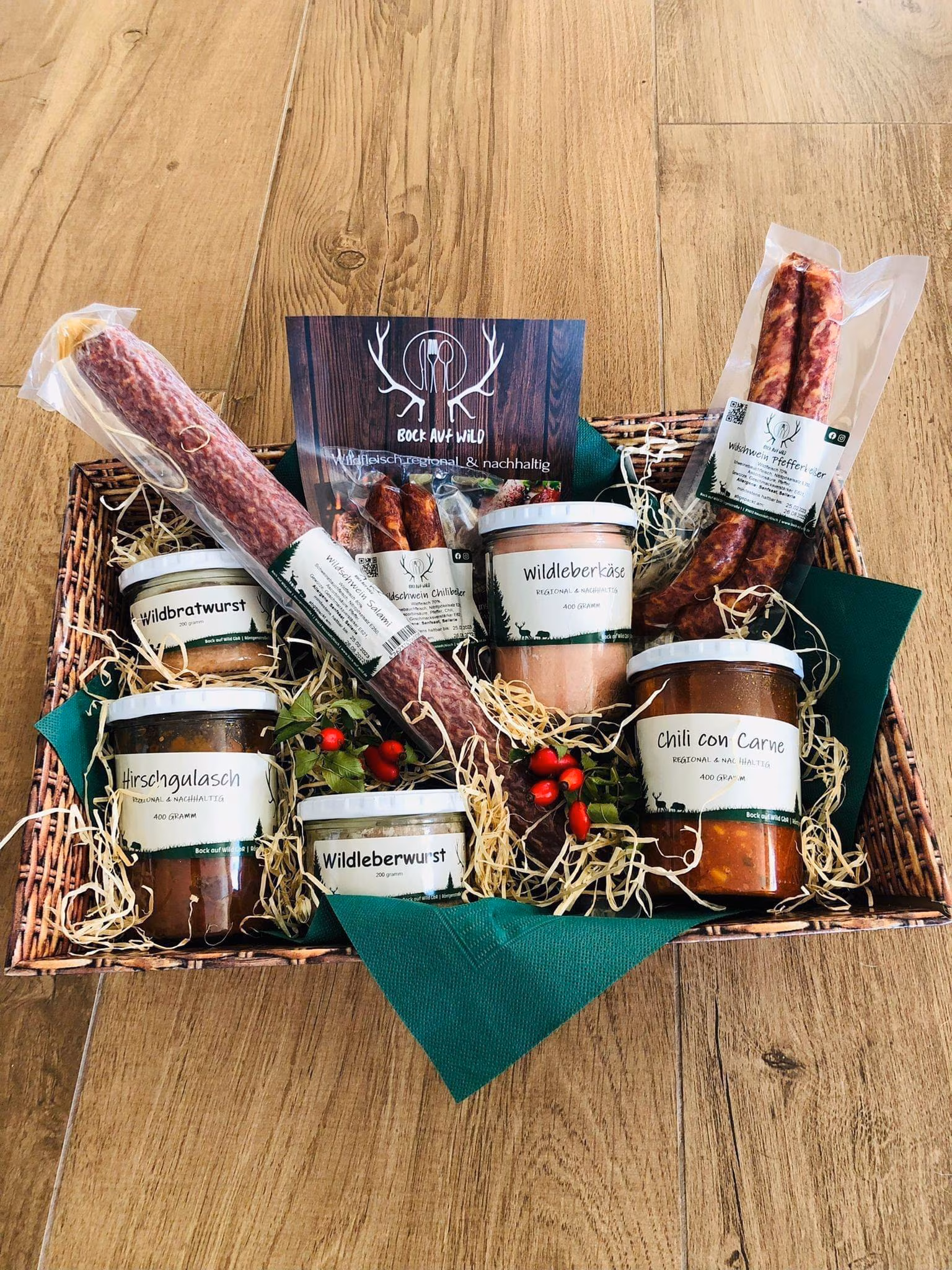 Geschenkkiste mit Würsten, Gläsern und Weihnachtsdekoration auf einem Holztisch