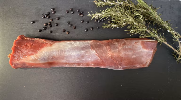 Rohes ausgelöstes Rückenstück mit Wacholderbeeren und Rosmarin auf einer Schieferplatte