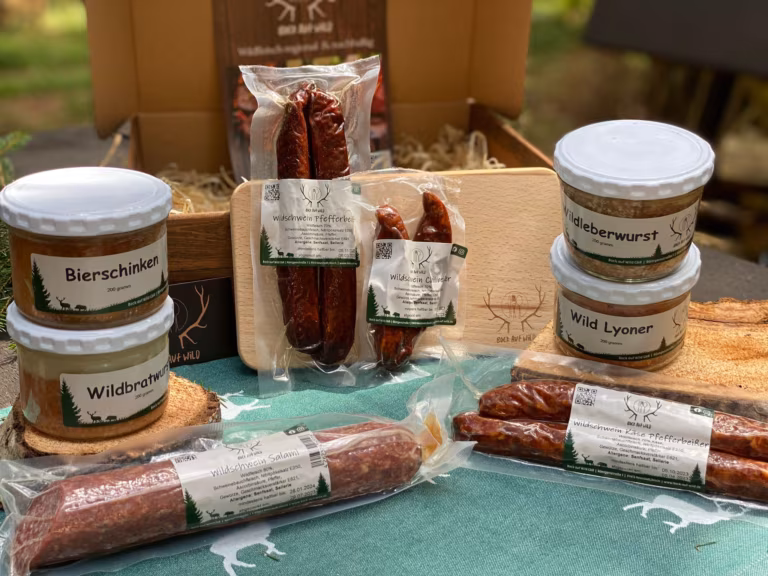 Brotzeitbox mit Holzbrett, Wurstgläsern und geräucherten Würsten vor einer Holzkiste