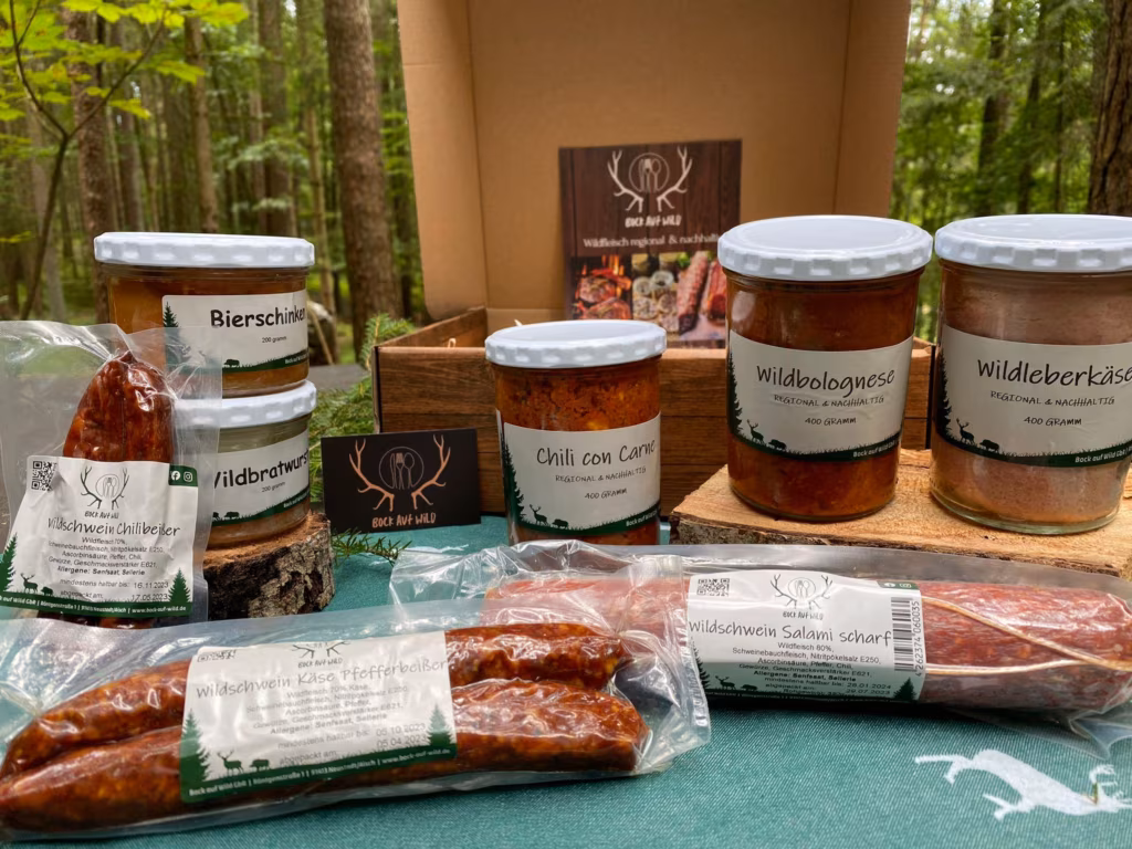 Probierpaket mit Wurstgläsern, Fertiggerichten und geräucherten Würsten vor einer Holzkiste im Wald