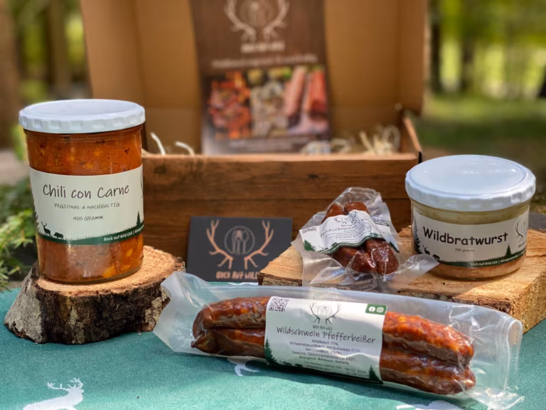 Kleines Probierpaket mit Chili con Carne, Wurstglas und geräucherten Würsten vor einer Holzkiste