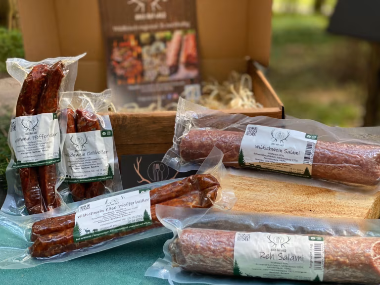 Geräucherte Würste und Salami in bedruckten Vakuumverpackungen auf grünem Tuch