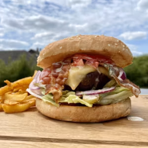 Burger mit Patty, Käse, Salat und Zwiebeln neben Pommes frites im Freien