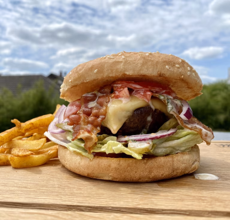 Burger mit Patty, Käse, Salat und Zwiebeln neben Pommes frites im Freien