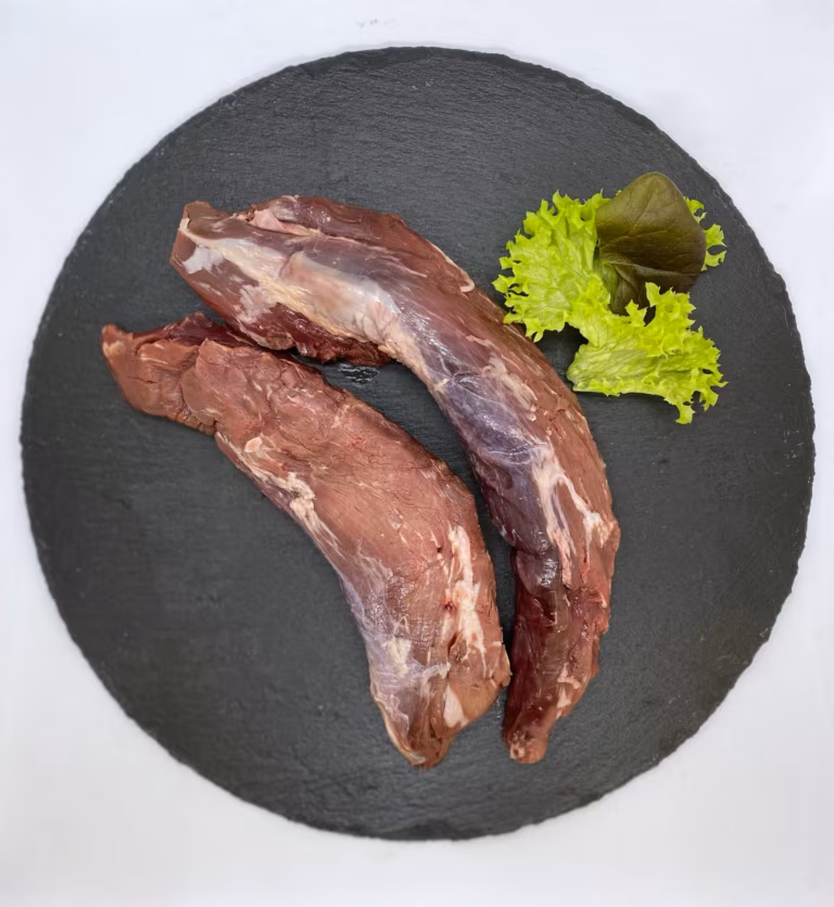 Zwei rohe Wildschweinfilets mit Salatgarnitur auf einer runden Schieferplatte