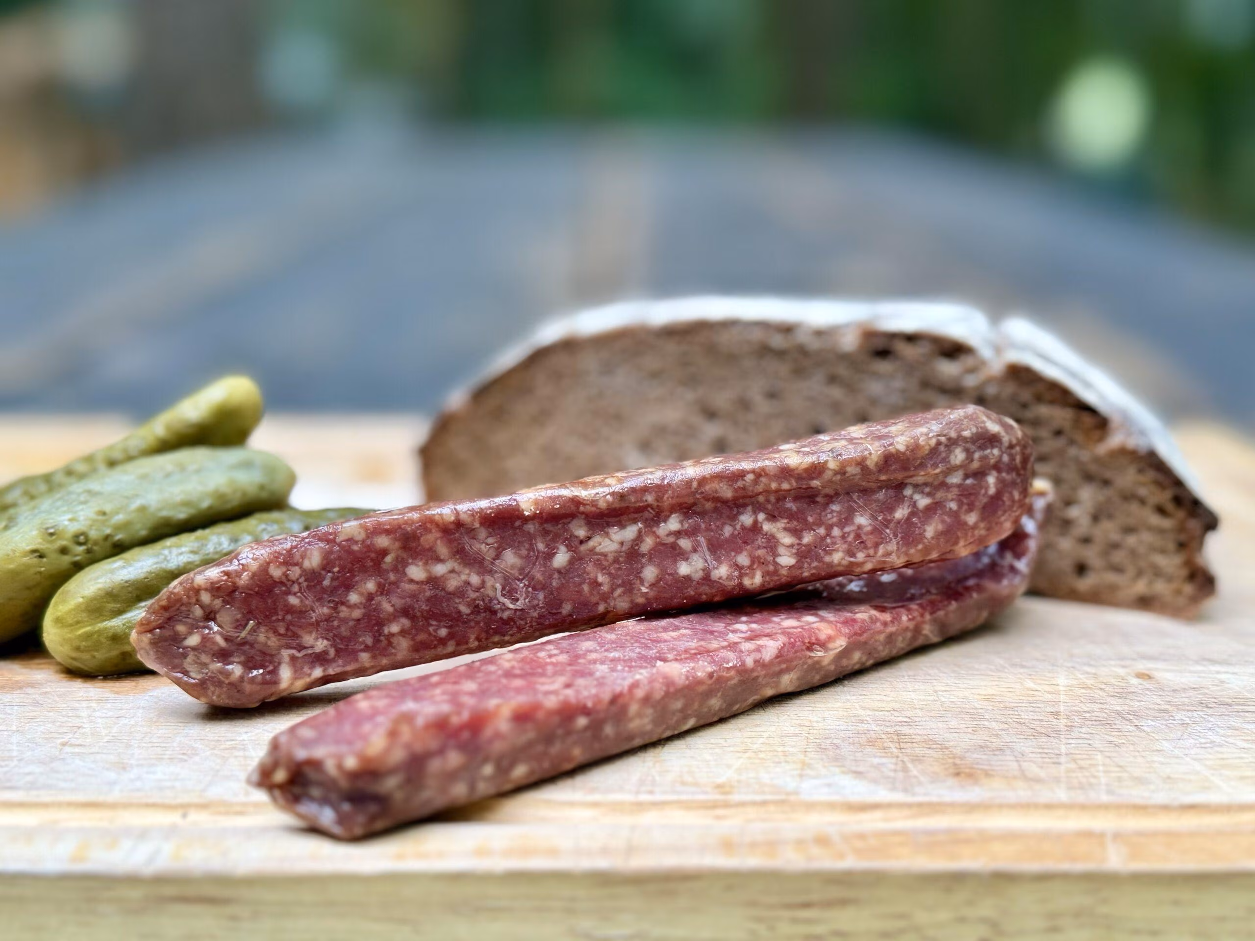 Zwei Landjäger neben Bauernbrot und Gewürzgurken auf einem Holzbrett
