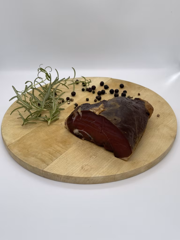 Stück Schinken mit Rosmarin und Wacholderbeeren auf einem runden Holzbrett